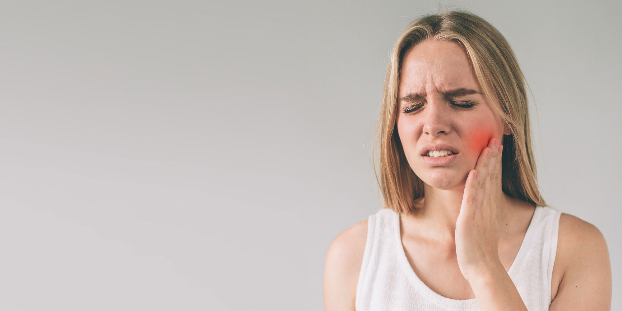 A woman holding her face in pain with one hand and the other hand up to her ear.