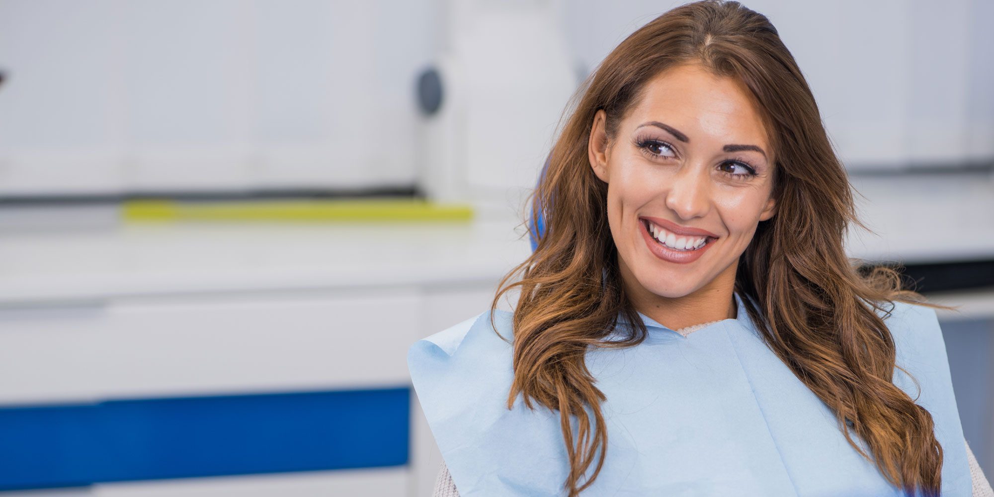 A woman smiles brightly while sitting in the dentist 's chair.