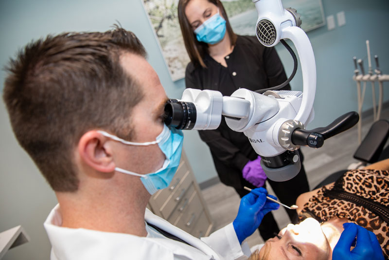 A man with glasses looking through the lens of an ophthalmoscope.