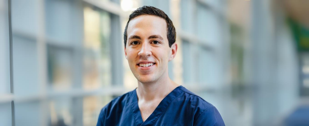 Smiling man in blue scrubs in a professional setting.